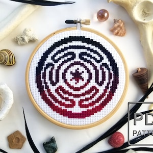 May include: A cross-stitch pattern of a red, purple and black labyrinth with a star in the centre. The pattern is framed in a wooden hoop. The text "PDF PATTERN" is visible in the bottom right corner of the image.
