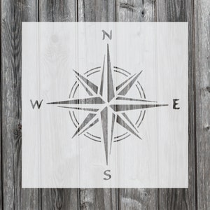 May include: A white stencil of a compass rose with the directions N, S, E, and W. The stencil is on a gray wood background.