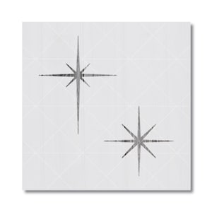 May include: A square stencil featuring two distinct starburst designs with elongated points. The starbursts are rendered in a dark, textured charcoal gray against a light gray background, which is overlaid with a faint white grid pattern.