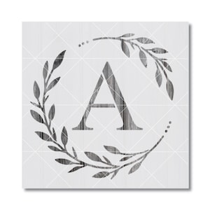 May include: A square sign featuring a dark gray letter A centered within a circular wreath of leaves. The design has a wood grain texture throughout, set against a light gray background with a faint white grid pattern overlaying the entire image.