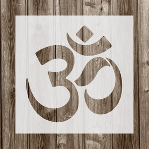 May include: A white stencil of the Om symbol, a sacred sound and spiritual icon in Hinduism, Buddhism, and Jainism. The stencil is on a square background, with a wooden plank background.