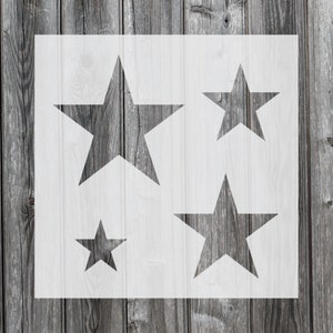 May include: A white stencil with four different sized star shapes cut out. The stencil is on a gray wood background.