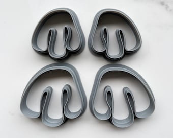 May include: Four gray plastic cookie cutters shaped like a stylized mushroom with a rounded top and a stem. The cutters are arranged in a square pattern.