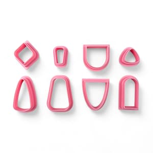 Puede incluir: Conjunto de ocho cortadores de galletas de plástico rosa en varias formas, incluyendo un diamante, un rectángulo, un triángulo, un corazón y algunas otras formas únicas.