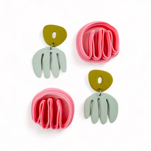 May include: A pair of earrings with a layered pink and green design. The earrings feature a layered pink design with a green accent. The earrings are made of polymer clay.