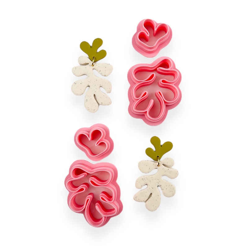 May include: Two pairs of pink and white layered leaf-shaped earrings with gold accents. The earrings are made of polymer clay and have a speckled finish.