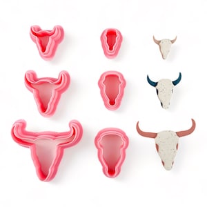 May include: Set of nine pink plastic cookie cutters shaped like bull skulls. The cutters are in various sizes and have a layered design.