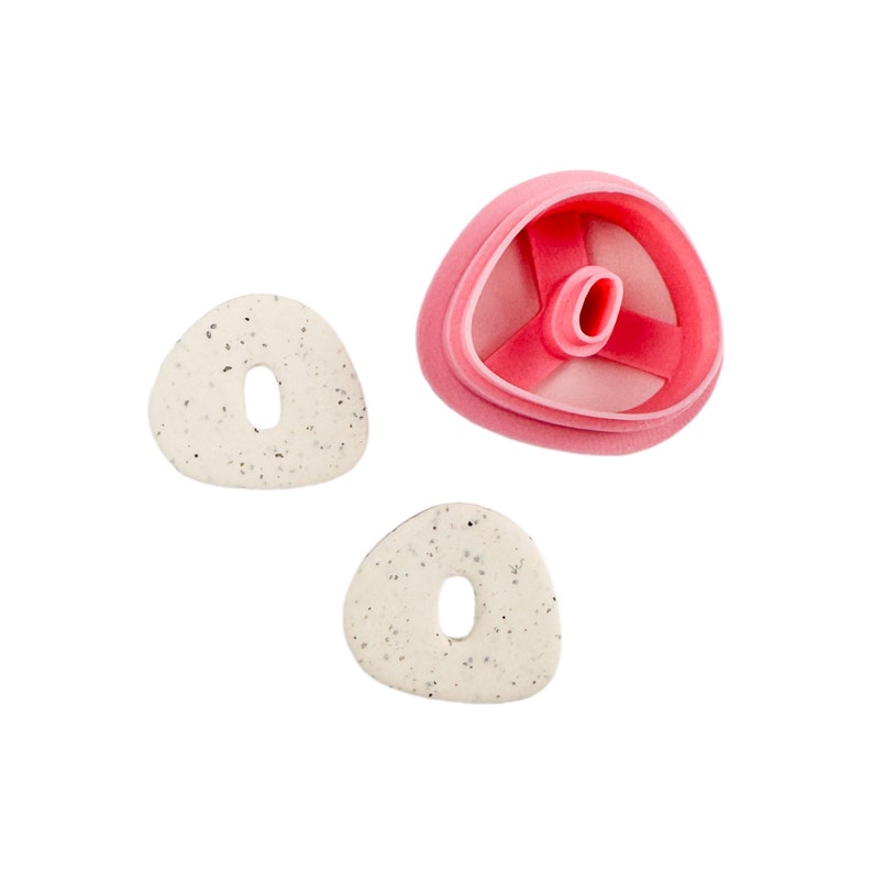 May include: Two white ceramic cookie cutters shaped like a rounded triangle with a hole in the center. A pink plastic cookie cutter shaped like a rounded triangle with a three-pronged design in the center.