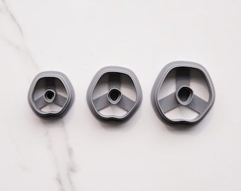 May include: Three gray plastic cookie cutters shaped like flowers with three petals and a center hole. The cutters are arranged in order of size from smallest to largest.