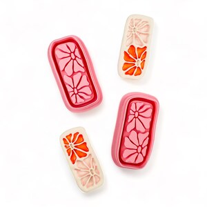 May include: Four pink and white rectangular ceramic tiles with floral designs. The tiles have a raised edge and a smooth surface. The flowers are in shades of pink and orange.