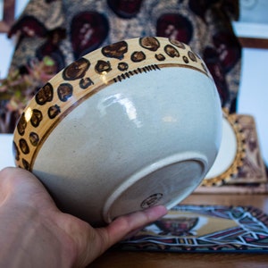 May include: A white ceramic bowl with a brown and tan leopard print design around the rim. The bowl is being held in a hand.
