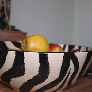 May include: A white ceramic bowl with black zebra stripes, filled with yellow and red apples.