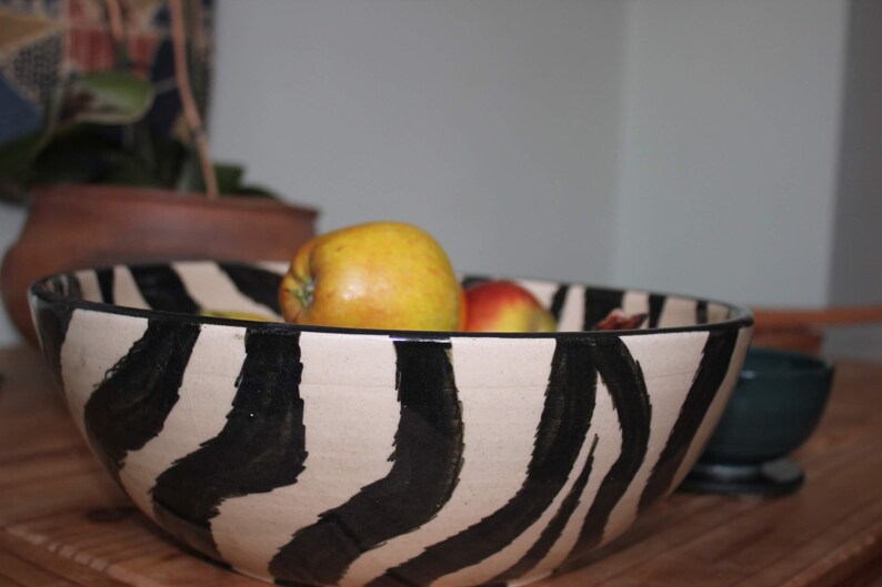May include: A white ceramic bowl with black zebra stripes, filled with yellow and red apples.