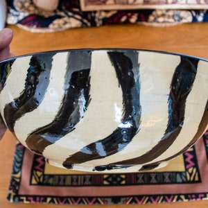 May include: A large, white ceramic bowl with black wavy stripes. The bowl is hand-painted and has a glossy finish.