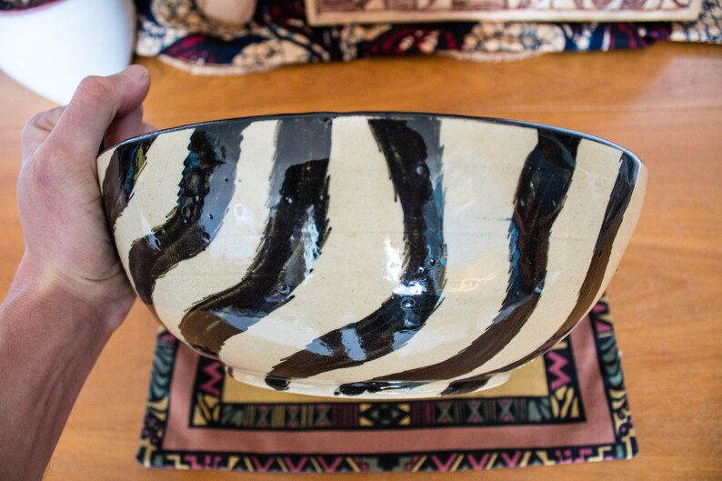 May include: A large, white ceramic bowl with black wavy stripes. The bowl is hand-painted and has a glossy finish.