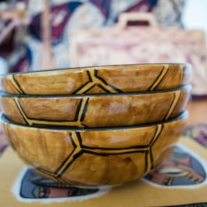 May include: A stack of four brown ceramic bowls with black geometric designs. The bowls are stacked on a colorful patterned surface.