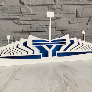 Pu&ograve; includere: Modello di stadio in legno bianco con accenti blu. Il modello &egrave; dettagliato con file di sedili e una torre centrale.
