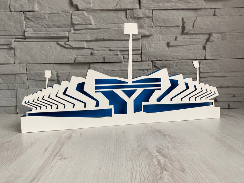 Pu&ograve; includere: Modello di stadio in legno bianco con accenti blu. Il modello &egrave; dettagliato con file di sedili e una torre centrale.