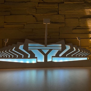 Pu&ograve; includere: Un modello di stadio in legno bianco illuminato con un interno blu. Il modello &egrave; illuminato dall'interno, creando un bagliore caldo.