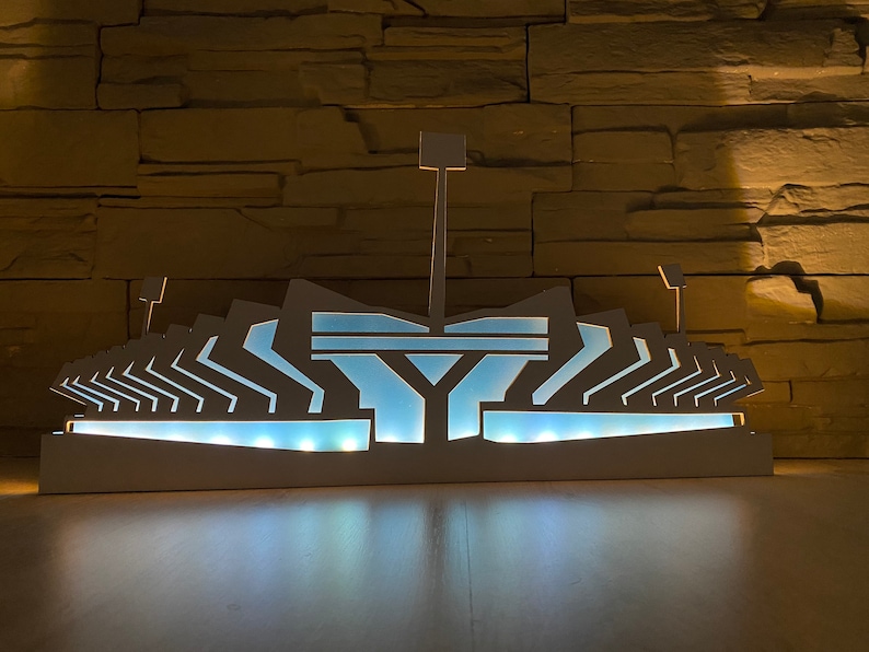 Pu&ograve; includere: Un modello di stadio in legno bianco illuminato con un interno blu. Il modello &egrave; illuminato dall'interno, creando un bagliore caldo.