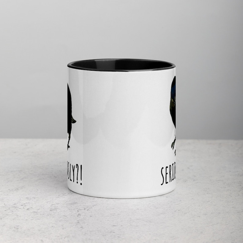 May include: White ceramic coffee mug with a black rim. The mug has a black and blue bird illustration on each side. The text "Seriously?!" is printed on the left side and "Seriously" is printed on the right side.