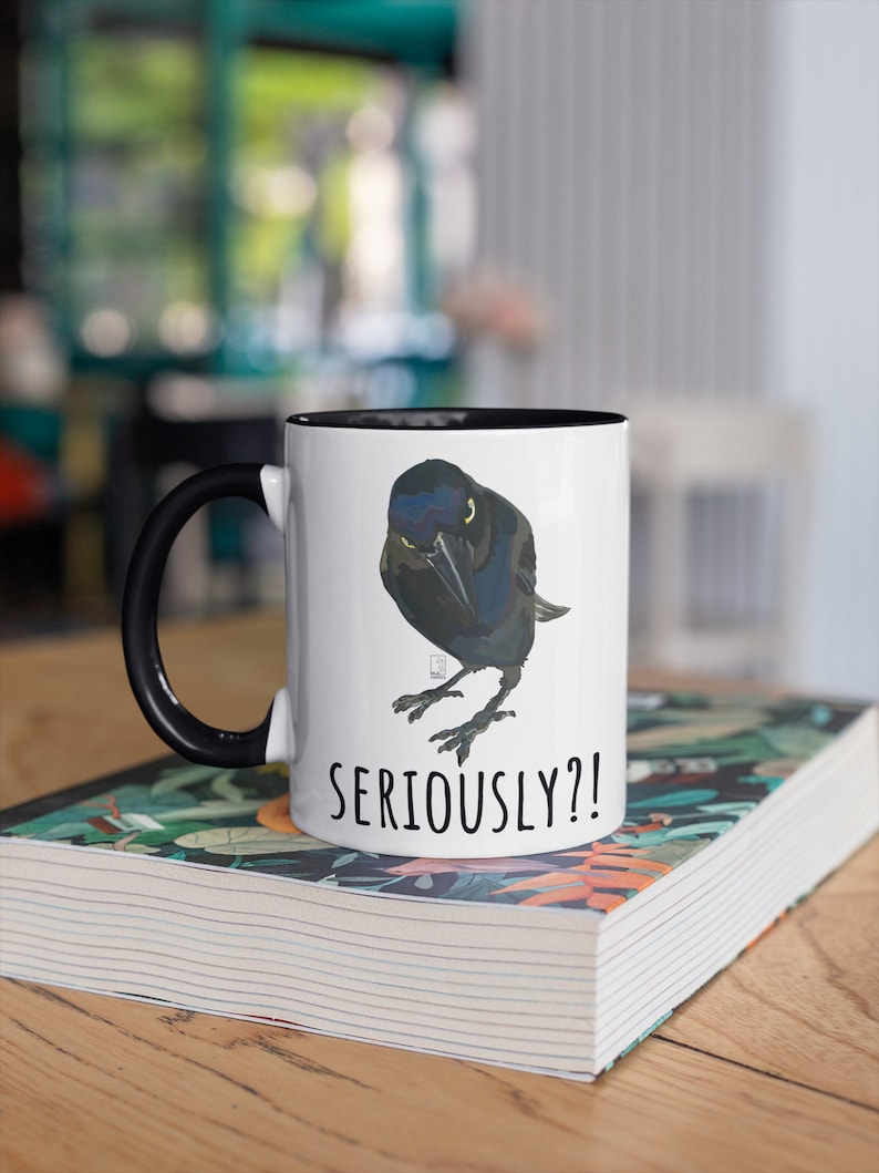 May include: White ceramic mug with a black rim and handle. The mug features a cartoon illustration of a black bird with the text "SERIOUSLY?!" printed below the bird.