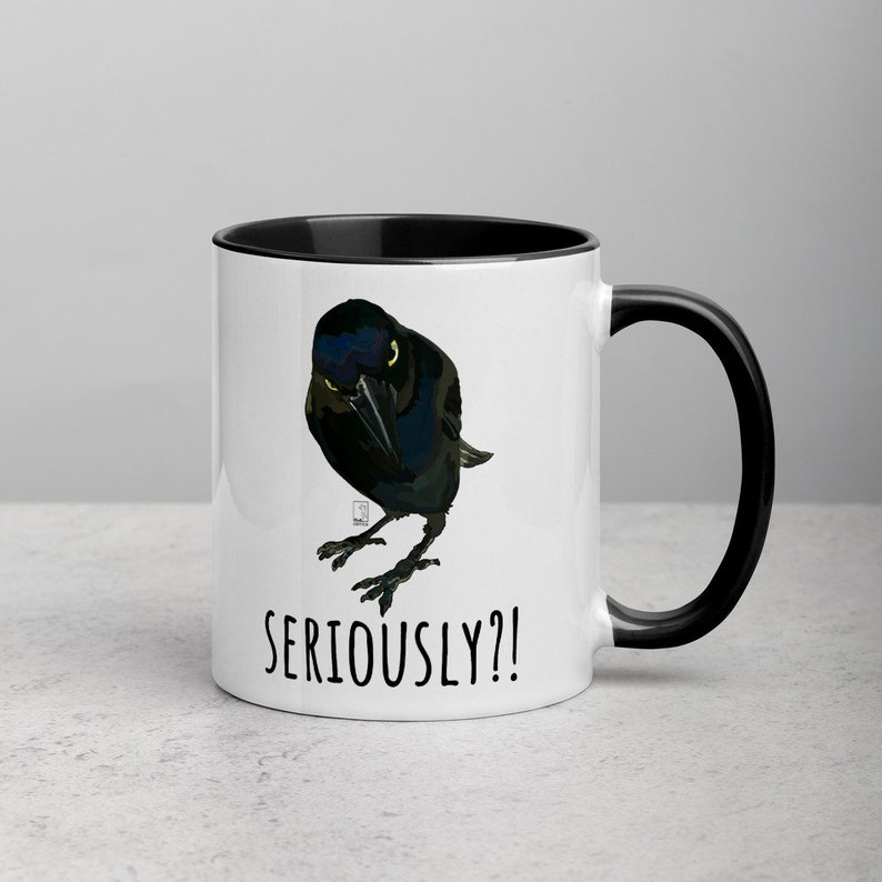 May include: White ceramic mug with a black rim and handle. The mug features a cartoon illustration of a black bird with a serious expression. The text "SERIOUSLY?!" is printed in black below the bird.
