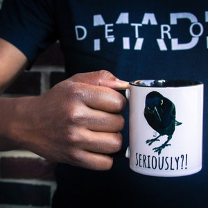 May include: White ceramic mug with a black rim and handle. The mug features a black and green illustration of a bird with the text "SERIOUSLY?!" printed below the bird.