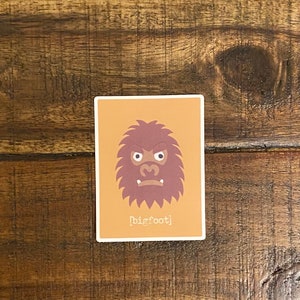 May include: A sticker with a cartoon illustration of Bigfoot's face on a light orange background. The text "[bigfoot]" is printed below the image.