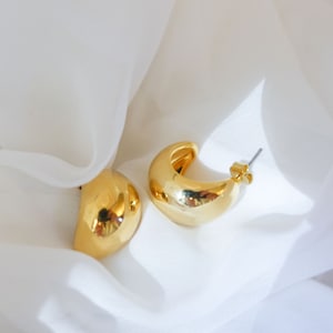 May include: A pair of gold hoop earrings with a rounded, slightly curved shape. The earrings are on a white background.