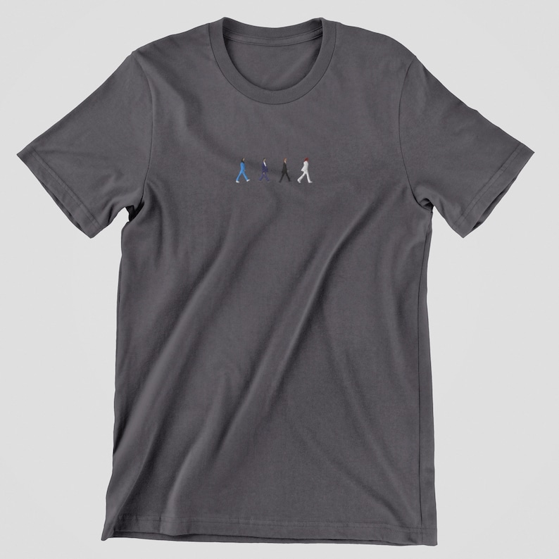 May include: A dark gray t-shirt with a small embroidered image of four figures walking across a street. The figures are wearing different colored clothing, including blue, black, and white.