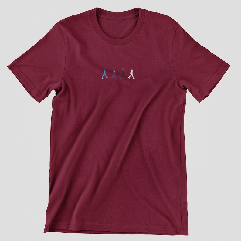 May include: A maroon t-shirt with a small embroidered image of four figures walking across a street, reminiscent of the iconic Abbey Road album cover.