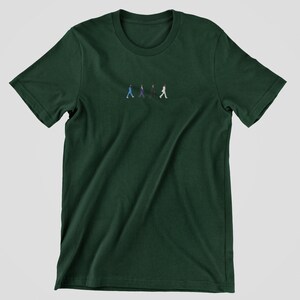 May include: A dark green t-shirt with a small embroidered image of four figures walking in a line. The figures are wearing different colored clothing.