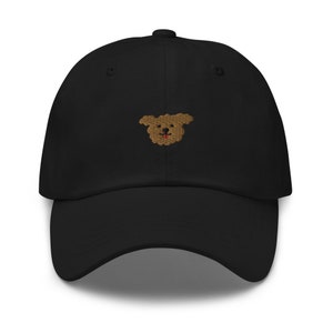 K&ouml;nnte beinhalten: Eine schwarze Baseballkappe mit einem gestickten braunen Hundegesicht auf der Vorderseite.