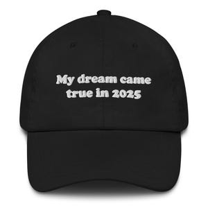 Könnte beinhalten: Schwarze Baseballkappe mit gebogenem Schirm. Auf der Kappe steht in weißer Schrift: "My dream came true in 2025". Die Kappe besteht aus einem weichen Material und hat einen verstellbaren Riemen.