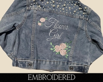 Könnte beinhalten: Eine blaue Jeansjacke mit Perlenbesatz am Kragen und bestickt mit dem Text "Flower Girl" und rosa Rosen.