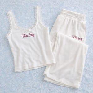 May include: A white pajama set comprising a vest top and shorts. The vest top has lace trim and the embroidered text "Mrs. Pong". The shorts have the embroidered date "5.28.2026". The set is made of a soft, ribbed material.