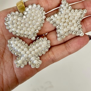 May include: Three white pearl and rhinestone embellishments in the shapes of a heart, a star, and a butterfly.