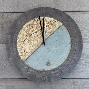 May include: A wooden clock with a nautical map design. The clock face features a map of a coastal area with a compass rose and the words "High Tide", "Low Tide", "Rising Tide", and "Falling Tide".
