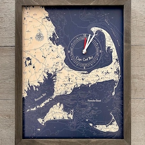 May include: A framed nautical map clock featuring a detailed map of Cape Cod Bay with a blue and beige color scheme. The clock face is centered on the bay and features a white clock hand and red hour hand.