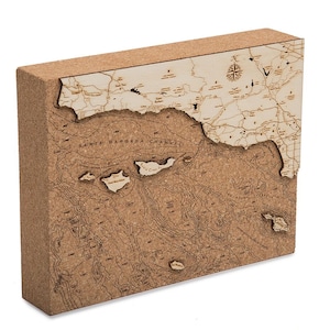 May include: A corkboard map of the Santa Barbara Channel, California, with a 3D relief design. The map shows the coastline, islands, and surrounding ocean depths. The map is made of cork and has a natural brown color.