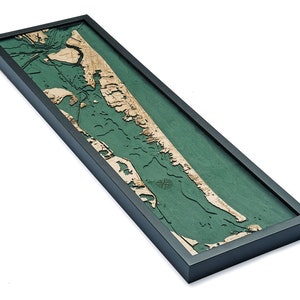 May include: A framed wooden map of the coastline of Long Island, New York. The map is made of wood and has a green background. The map is framed in a black frame.