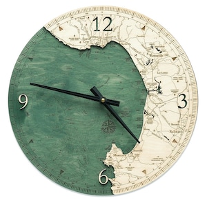 May include: A green and brown wooden clock with a map of the Monterey Bay area. The clock face has black hands and Roman numeral markings. The clock is 12 inches in diameter.
