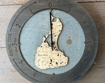 Op de afbeelding: Een houten getijdenklok met een kaart van Block Island, Rhode Island. De wijzerplaat van de klok is grijs met witte markeringen en de cijfers 1 tot en met 5. De wijzers van de klok zijn zwart. De klok is ingesteld op hoogwater.