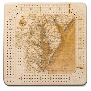 May include: A wooden cribbage board with a map of the Chesapeake Bay engraved on the surface. The board has a compass rose and the words "Chesapeake Bay" printed on it. The board is made of light wood and has a natural finish.