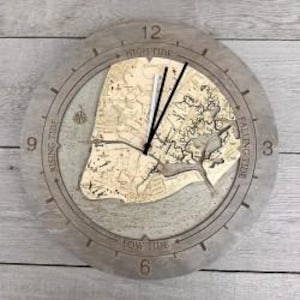 May include: A round wooden wall clock featuring a light-colored wood map inlay of a coastal area. The clock face has engraved text reading High Tide, Rising Tide, Falling Tide, and Low Tide, with black and silver hands and a compass rose icon.