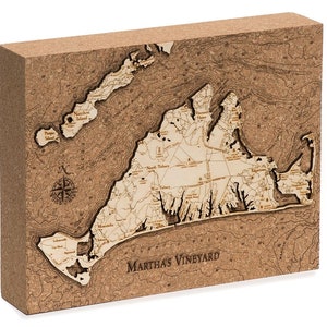 May include: A cork map of Martha's Vineyard, a popular island destination off the coast of Massachusetts. The map is made of cork and features a detailed outline of the island, including its towns, roads, and waterways. The map is mounted on a wooden base and has a compass rose in the lower left corner.