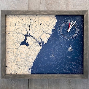 May include: A framed nautical map clock with a blue and white color scheme. The clock face features a compass rose and the words "High Tide" and "Low Tide". The map shows a coastal area with a compass rose in the lower right corner.