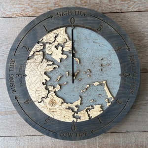 May include: A wooden tide clock with a nautical map of Boston Harbor. The clock face is divided into 12 hours, with the numbers 1 through 5 and the words "High Tide" and "Low Tide" marked. The clock hands are black and point to the current tide level.