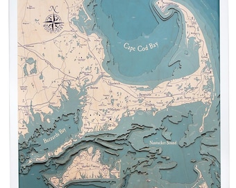 May include: A framed 3D wooden map of Cape Cod, Massachusetts, with detailed topographical features. The map features the text "WOOD CHART" and a compass rose. The water is a teal color, and the land is a light wood color.